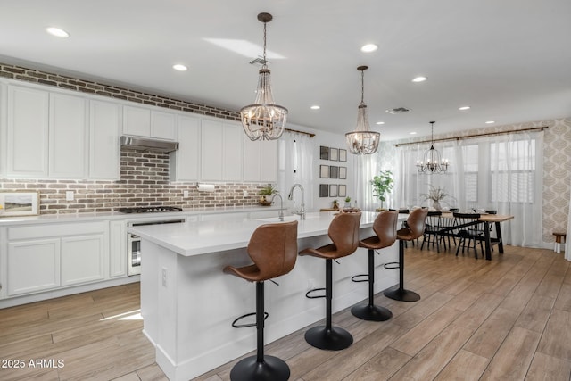 kitchen with hanging light fixtures, a kitchen island with sink, white cabinets, sink, and a breakfast bar area