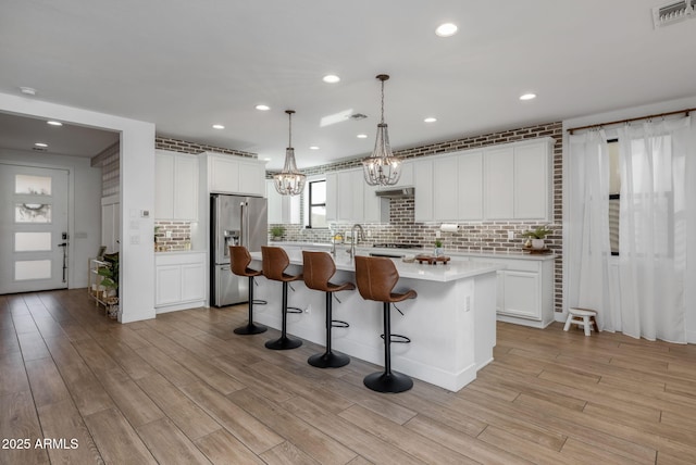 kitchen featuring white cabinetry, hanging light fixtures, high end refrigerator, and a kitchen island with sink