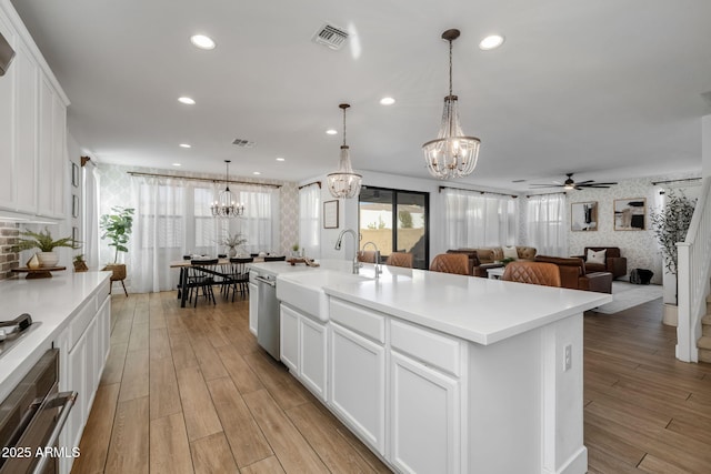 kitchen featuring light hardwood / wood-style floors, white cabinetry, hanging light fixtures, an island with sink, and stainless steel appliances