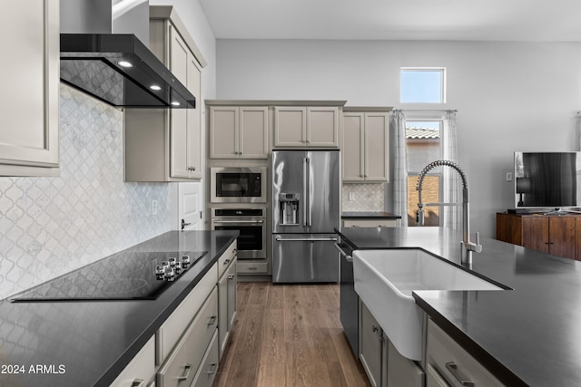 kitchen with wall chimney exhaust hood, gray cabinets, appliances with stainless steel finishes, and dark hardwood / wood-style flooring