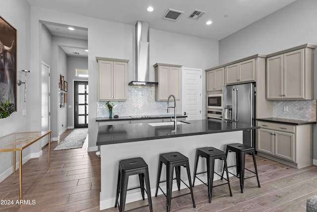 kitchen with wall chimney exhaust hood, gray cabinets, stainless steel appliances, a breakfast bar area, and hardwood / wood-style floors