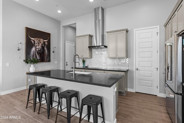 kitchen featuring an island with sink, gray cabinetry, dark wood-type flooring, wall chimney range hood, and high end refrigerator