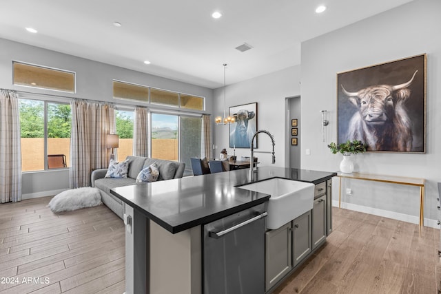 kitchen with light wood-type flooring, a center island with sink, sink, and stainless steel dishwasher