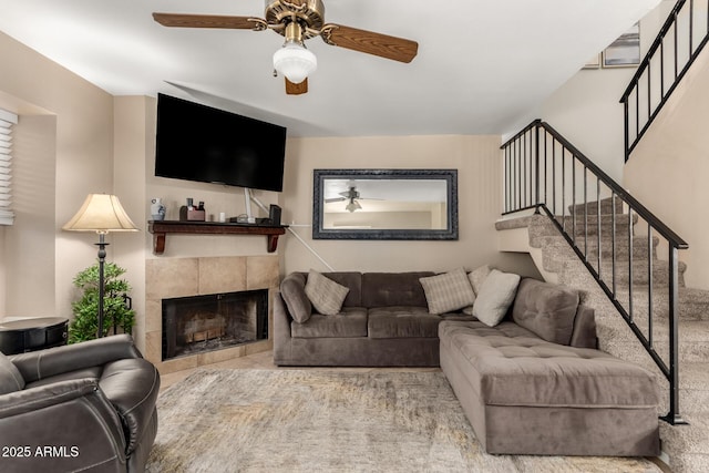 living room with a ceiling fan, a tiled fireplace, and stairs