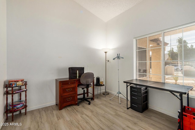 office featuring lofted ceiling, light wood-style flooring, baseboards, and a textured ceiling