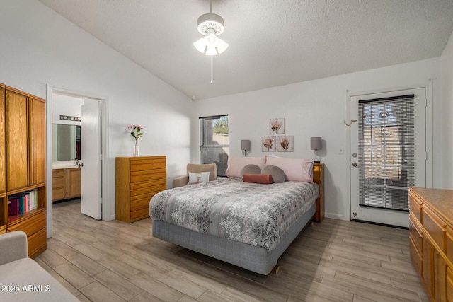 bedroom with lofted ceiling, connected bathroom, light wood-style flooring, and a textured ceiling