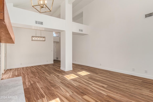 unfurnished living room with an inviting chandelier, a towering ceiling, and hardwood / wood-style floors