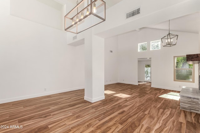 unfurnished living room featuring a towering ceiling, hardwood / wood-style floors, and an inviting chandelier