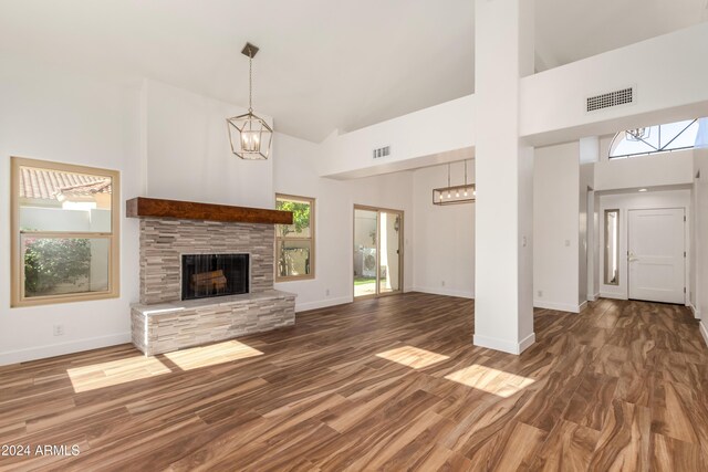 unfurnished living room featuring dark hardwood / wood-style floors, a towering ceiling, a stone fireplace, and a notable chandelier