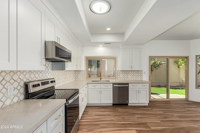 kitchen with a raised ceiling, backsplash, white cabinets, light stone counters, and stainless steel appliances