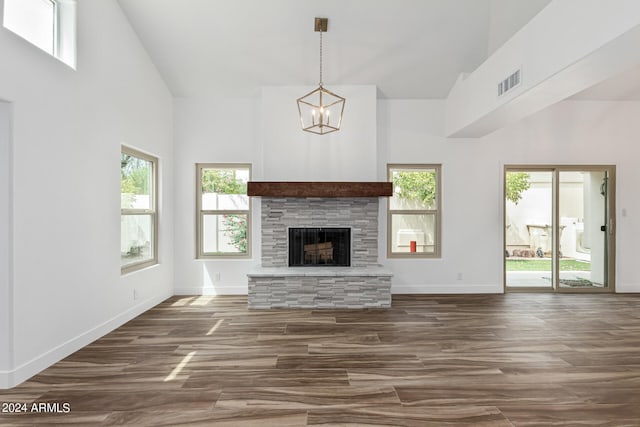 unfurnished living room featuring dark hardwood / wood-style floors, a healthy amount of sunlight, a stone fireplace, and a chandelier