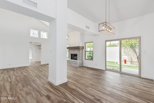 unfurnished living room with a stone fireplace, a chandelier, high vaulted ceiling, and light hardwood / wood-style flooring