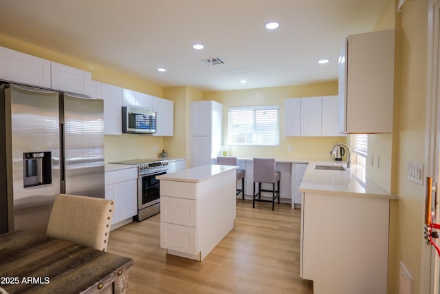 kitchen with sink, appliances with stainless steel finishes, white cabinets, a kitchen island, and light wood-type flooring