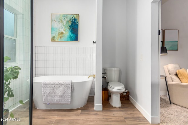 bathroom with wood-type flooring, toilet, tile walls, and a tub