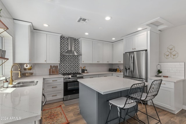 kitchen featuring wall chimney exhaust hood, sink, a center island, stainless steel appliances, and white cabinets