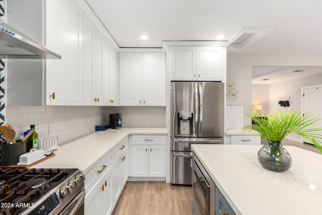 kitchen featuring white cabinetry, stainless steel fridge, light stone counters, and wall chimney range hood