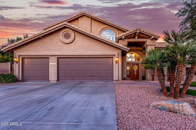 view of front facade with stucco siding, a garage, driveway, and a tile roof