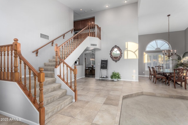 staircase with a notable chandelier, visible vents, baseboards, and a towering ceiling