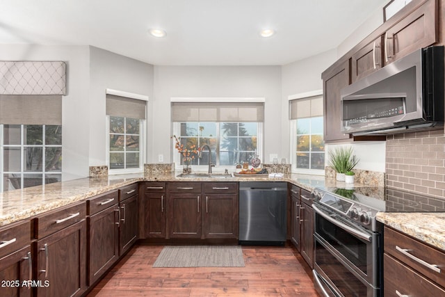 kitchen featuring a sink, light stone counters, backsplash, wood finished floors, and stainless steel appliances