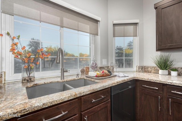 kitchen with dark brown cabinetry, dishwashing machine, light stone counters, and a sink