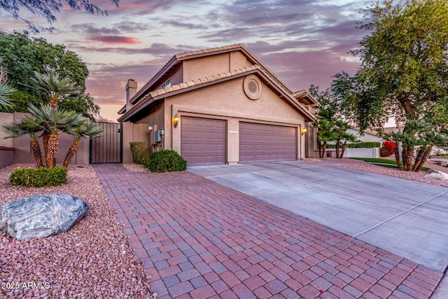 view of front facade featuring fence, stucco siding, a garage, driveway, and a gate