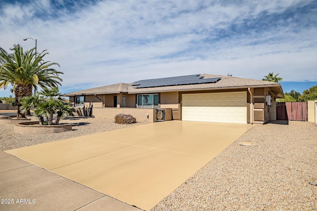 view of front of home with stucco siding, solar panels, concrete driveway, an attached garage, and fence