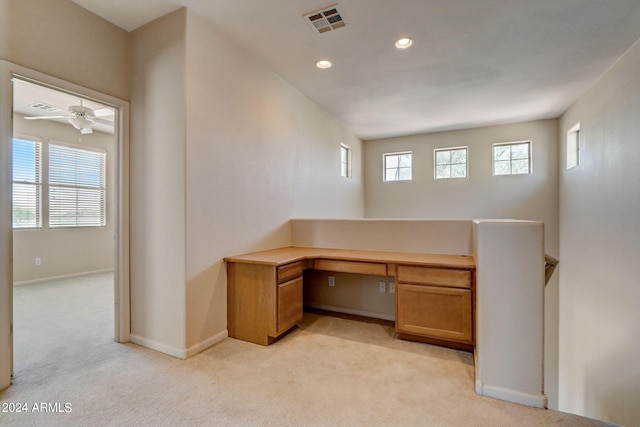 unfurnished office featuring built in desk, light colored carpet, plenty of natural light, and ceiling fan