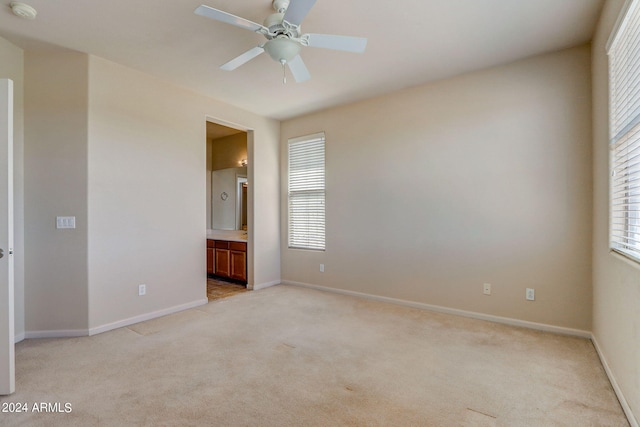 unfurnished bedroom with light colored carpet, ensuite bath, and ceiling fan