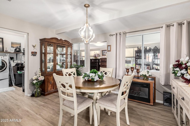 dining room featuring washer / dryer, beam ceiling, light hardwood / wood-style floors, and a chandelier