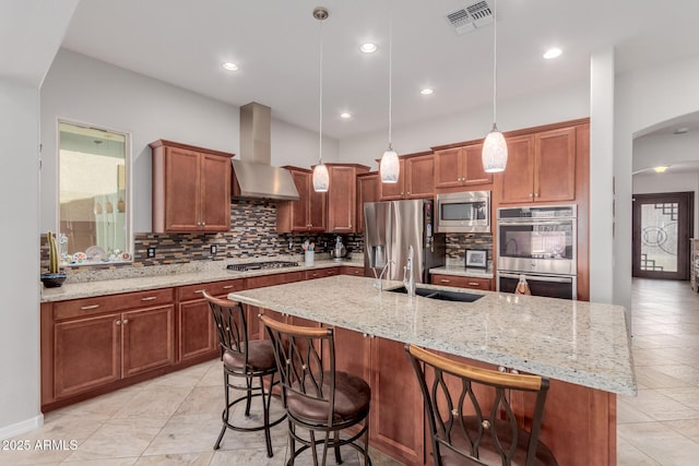 kitchen featuring arched walkways, stainless steel appliances, a sink, visible vents, and wall chimney range hood