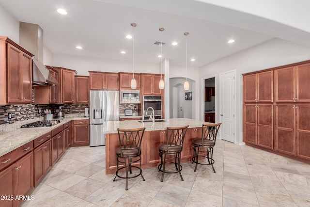 kitchen with arched walkways, decorative backsplash, an island with sink, stainless steel appliances, and a sink