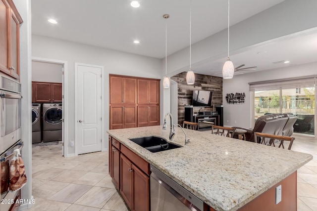 kitchen featuring open floor plan, independent washer and dryer, hanging light fixtures, stainless steel dishwasher, and a sink