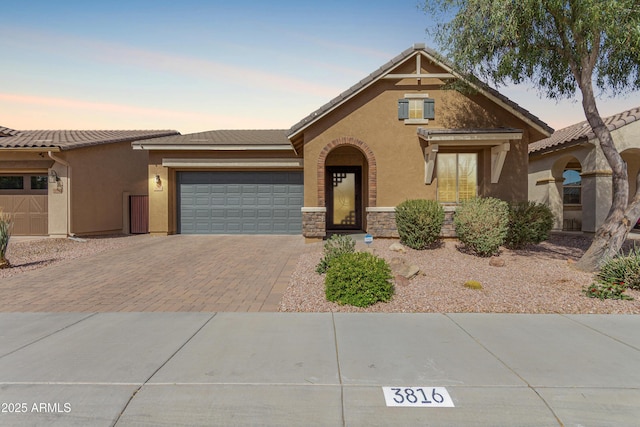 view of front facade featuring a tiled roof, decorative driveway, an attached garage, and stucco siding