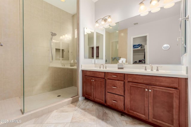 bathroom featuring a walk in closet, a sink, a tile shower, and double vanity