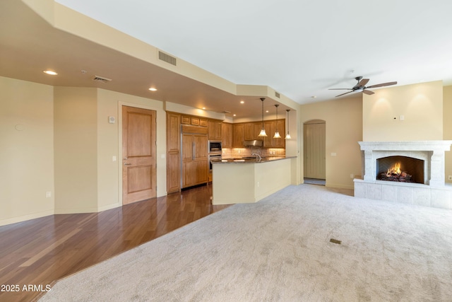 unfurnished living room with ceiling fan, sink, a tiled fireplace, and dark carpet