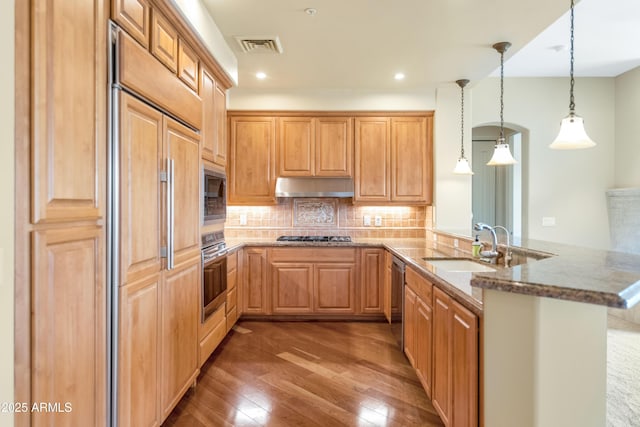 kitchen featuring built in appliances, decorative backsplash, dark hardwood / wood-style flooring, decorative light fixtures, and kitchen peninsula