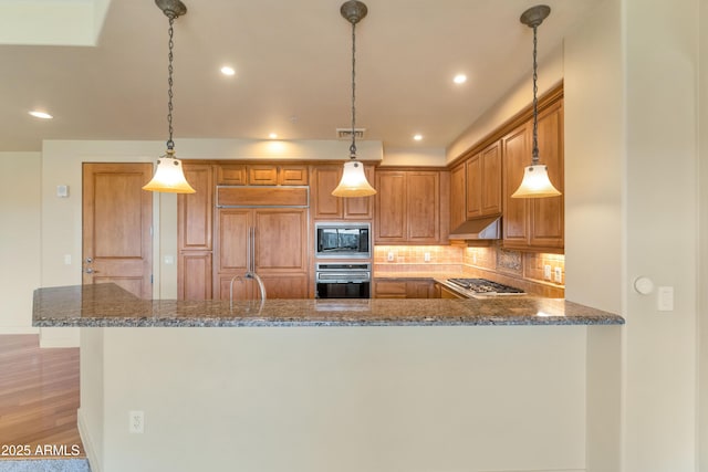 kitchen featuring built in appliances, dark stone countertops, kitchen peninsula, pendant lighting, and backsplash