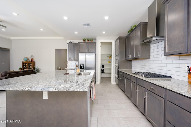 kitchen featuring wall chimney exhaust hood, backsplash, a center island with sink, sink, and appliances with stainless steel finishes