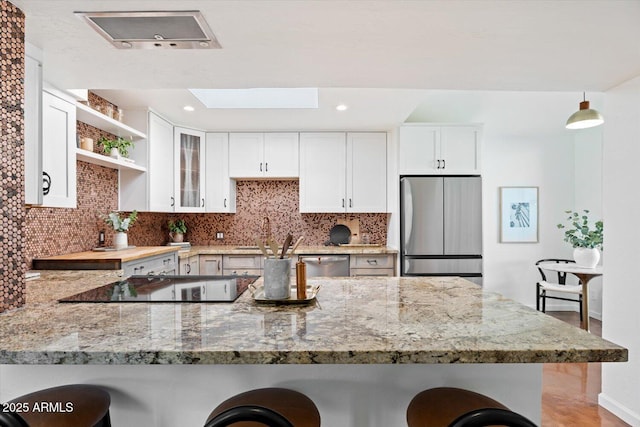 kitchen featuring stainless steel appliances, kitchen peninsula, white cabinets, and a kitchen bar