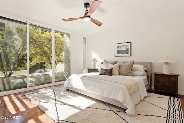 bedroom featuring access to exterior, wood-type flooring, expansive windows, and ceiling fan