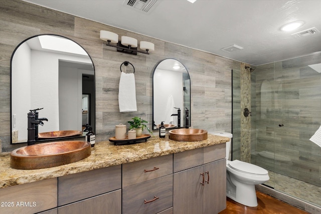 bathroom featuring walk in shower, vanity, toilet, and tile walls