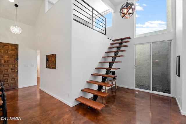 staircase with a towering ceiling, concrete floors, and a notable chandelier