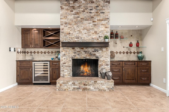 bar with tasteful backsplash, dark brown cabinetry, beverage cooler, and stone counters