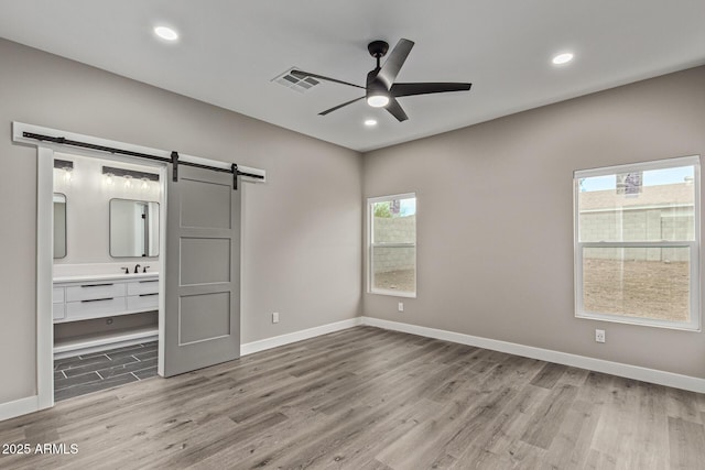 unfurnished bedroom featuring recessed lighting, baseboards, a barn door, and wood finished floors