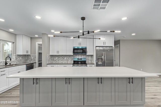 kitchen featuring visible vents, gray cabinets, light wood-style floors, stainless steel appliances, and a sink