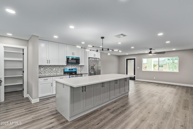 kitchen featuring visible vents, backsplash, a kitchen island, light countertops, and stainless steel appliances