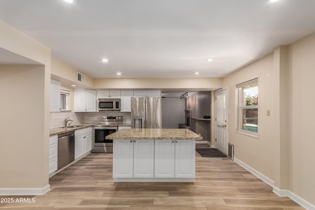 6009 W Medlock Dr, Glendale, AZ 85301 - kitchen with stainless steel appliances, a kitchen island, white cabinetry, light wood-style flooring, and light stone counters