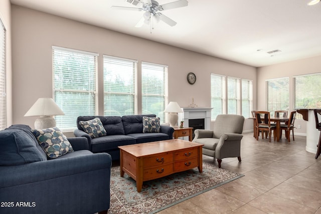 living area with light tile patterned floors, baseboards, visible vents, a ceiling fan, and a fireplace