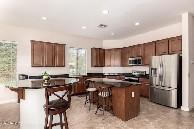 kitchen featuring appliances with stainless steel finishes, a breakfast bar, a sink, and a center island