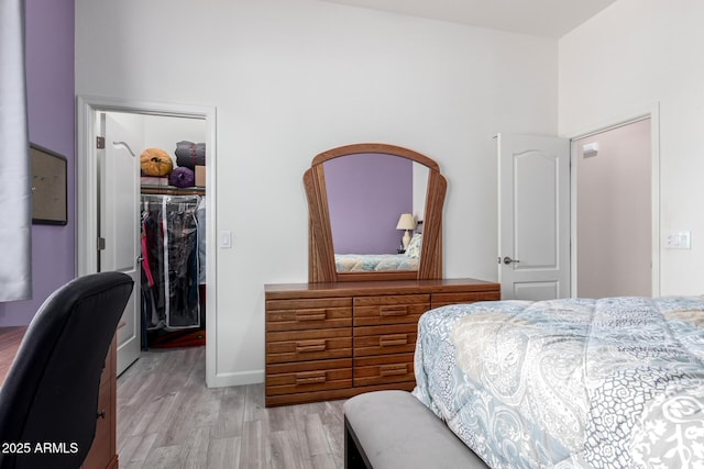 bedroom featuring light wood-style floors, a walk in closet, a closet, and baseboards